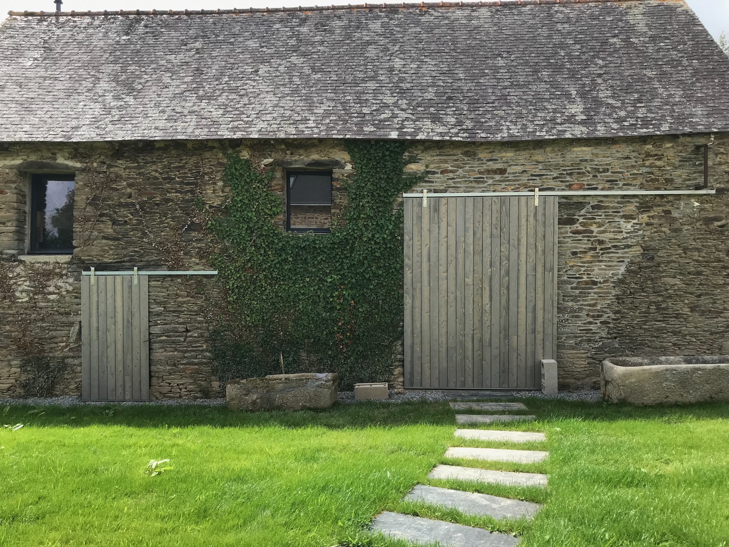 Large slate slabs form meadering path between main house and guest accommodation. Large metal framed sliding shutters to converted barn openings