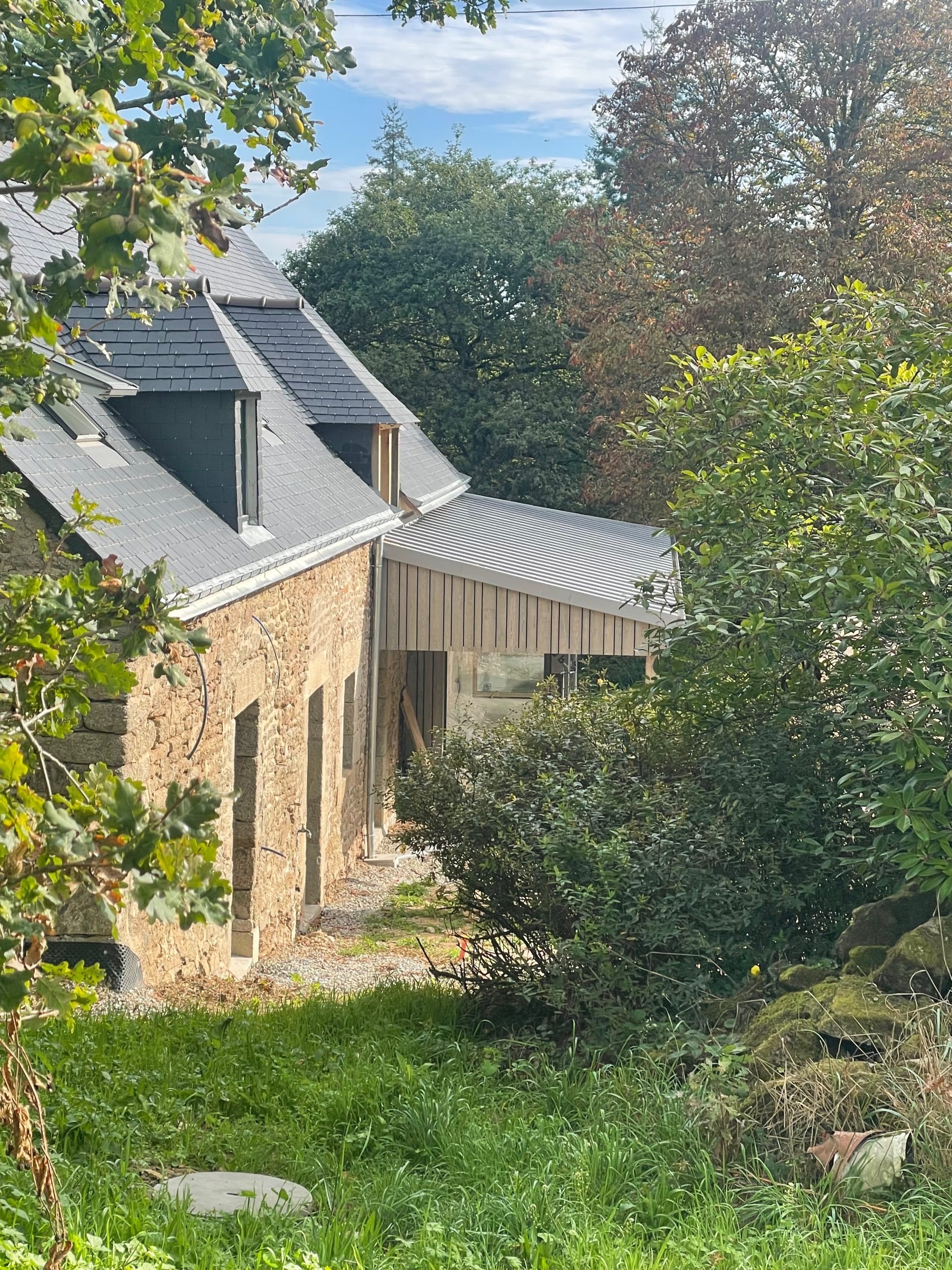 external view showing chestnut cladding and standing seam zinc roof of the extension to a stone longère