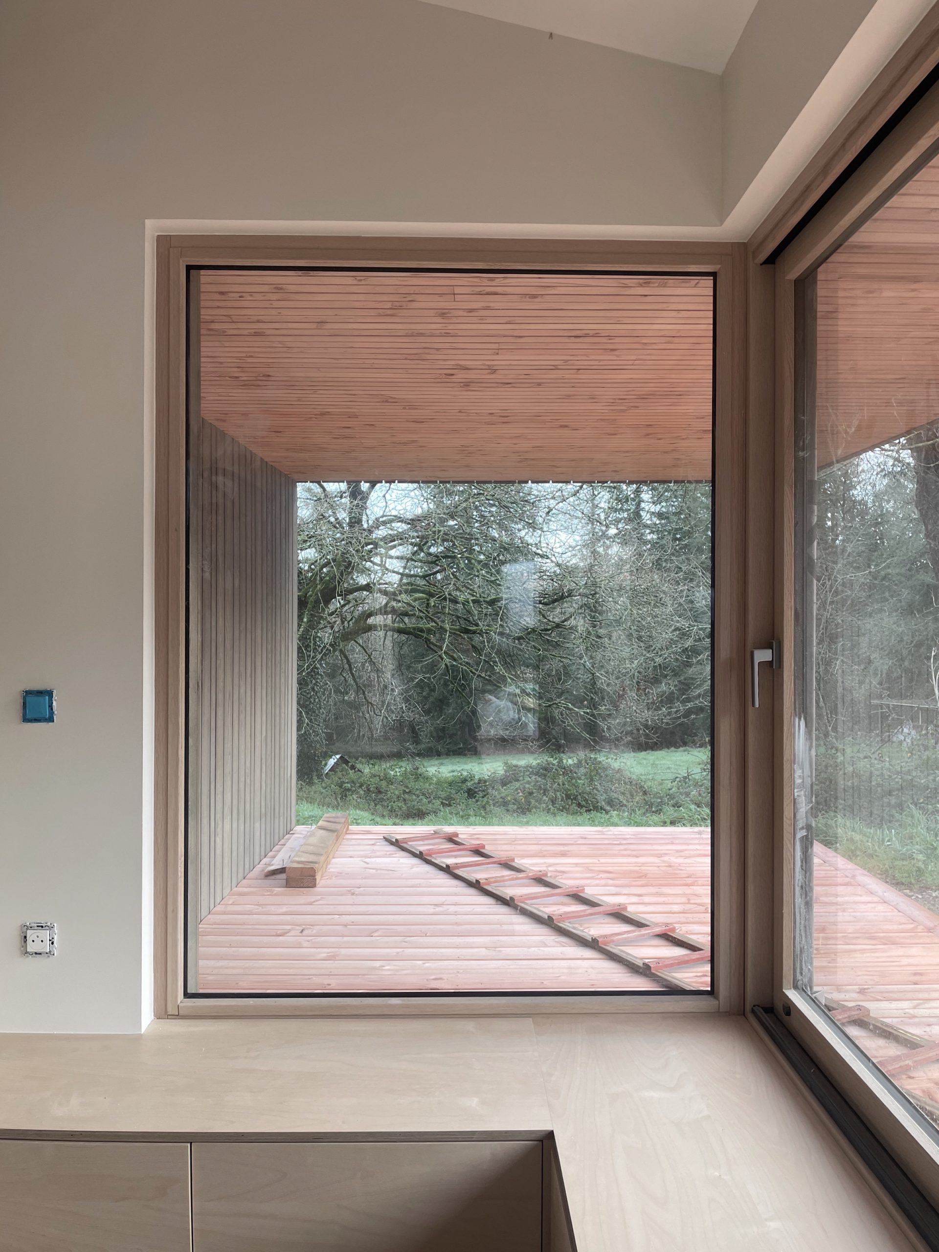 A bay-style window protrudes from the façade, featuring full-height glazing from built-in seating to ceiling, offering expansive views across the garden.